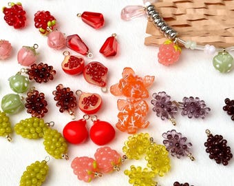 Può includere: Una collezione di ciondoli e perline a forma di frutta colorata in varie dimensioni e colori. I ciondoli includono fragole, uva, melograni e altri frutti. Alcuni ciondoli hanno anelli in metallo color oro per il fissaggio a gioielli o altri lavori artigianali.