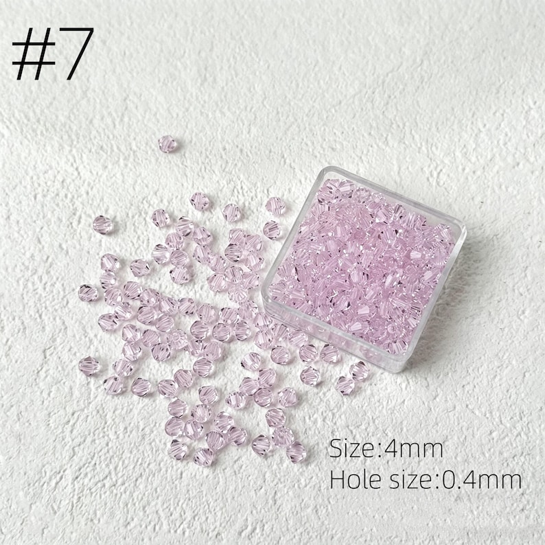May include: A collection of light purple crystal beads, 4mm in size, with a 0.4mm hole, are scattered on a white surface. Some beads are contained in a clear square container. The number "7" is in the upper left corner.