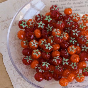 Peut inclure: Un bol en verre transparent rempli de nombreuses petites perles de citrouille en verre dans des tons orange et rouge. Chaque perle a des détails de feuilles vertes. Les perles varient en taille et sont dispersées dans le bol, créant un thème d'automne festif.