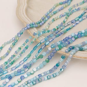 Peut inclure: Plusieurs brins de perles de verre bleues et vertes de différentes formes et tailles. Les perles comprennent des formes rondes, ovales et carrées, certaines étant facettées. La palette de couleurs varie du turquoise clair au bleu océan profond.