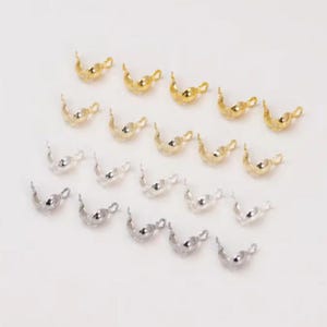 Peut inclure: Collection de petites fournitures de bijoux dorées et argentées, disposées sur une surface blanche. Les fournitures ont une forme incurvée avec une boucle à une extrémité, pour la fabrication de bijoux.
