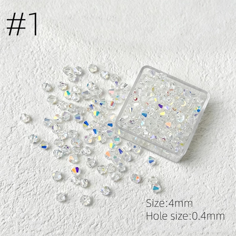 May include: Clear, iridescent crystal beads scattered on a white surface, with some contained in a clear square container. The text "#1" is in the upper left corner. The text "Size: 4mm" and "Hole size: 0.4mm" are in the lower right corner.