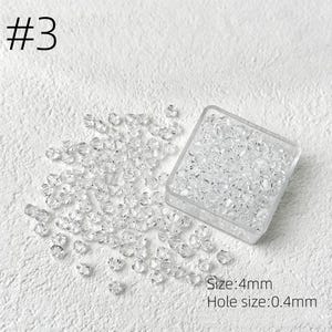 May include: Clear crystal beads, size 4mm, are scattered on a white surface, with some contained in a clear square container. The text "#3" is in the upper left corner. The text "Size: 4mm" and "Hole size: 0.4mm" are in the lower right corner.