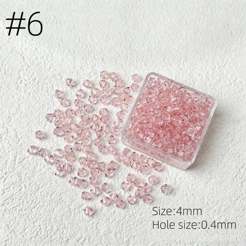 May include: Pink crystal beads, size 4mm, are scattered on a white surface, with some contained in a clear plastic square container. The hole size is 0.4mm. The number 6 is in the upper left corner.