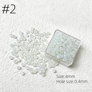 May include: A collection of small, clear, faceted beads, some scattered and some contained in a clear square container. The text "#2" is in the upper left corner. The text "Size: 4mm" and "Hole size: 0.4mm" are in the lower right corner.