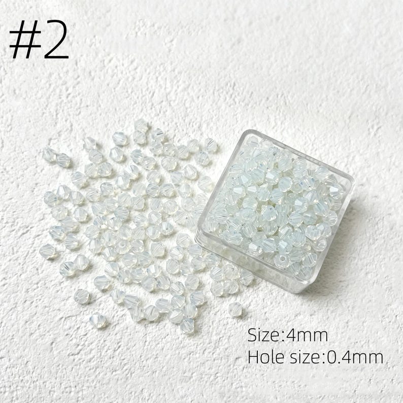 May include: A collection of small, clear, faceted beads, some scattered and some contained in a clear square container. The text "#2" is in the upper left corner. The text "Size: 4mm" and "Hole size: 0.4mm" are in the lower right corner.