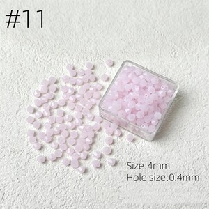 May include: A collection of light pink faceted beads, scattered on a white surface, with some contained in a clear plastic box. The text "#11" is in the upper left corner. The text indicates the beads are 4mm in size with a 0.4mm hole.