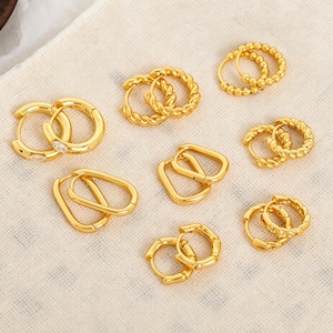Può includere: Una collezione di orecchini a cerchio color oro in vari stili, inclusi cerchi rotondi lisci, cerchi con texture a corda intrecciata, cerchi rettangolari e cerchi con perline, tutti dotati di chiusure a cerniera.