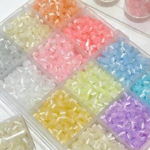 May include: A clear plastic organizer filled with various colors of small, round beads. The beads are in shades of white, yellow, orange, pink, blue, green, and purple. The beads are likely for crafting or jewelry making.