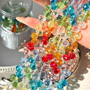 May include: A collection of multi-coloured faceted glass beads arranged in several vertical strands. The beads feature a variety of vibrant hues including red, orange, yellow, green, blue, and clear tones, all reflecting light with a polished finish.