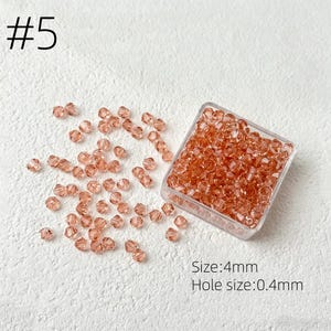 May include: A collection of small, faceted, peach-colored beads, some scattered and some contained in a clear square container. The text "#5" is in the upper left corner. The text "Size: 4mm" and "Hole size: 0.4mm" are in the lower right corner.