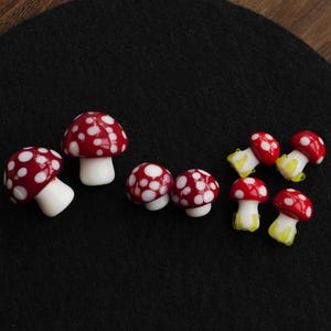 Pode incluir: Uma coleção de figuras de cogumelos de vidro. Os cogumelos têm chapéus vermelhos com manchas brancas e caules brancos ou amarelos. As figuras estão dispostas sobre uma superfície preta.