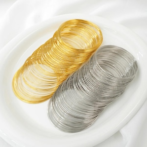 Puede incluir: Dos montones de anillos de alambre, uno dorado y otro plateado, se disponen sobre un plato blanco. Los anillos, enrollados con fuerza, se colocan con los dorados a la izquierda y los plateados a la derecha. El fondo es de tela blanca.