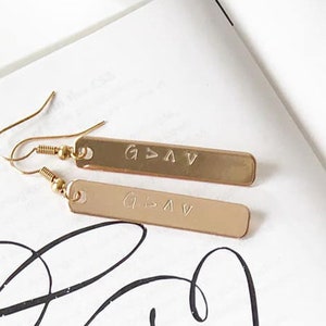 May include: Gold bar earrings with the word "G.L.A.V." engraved on each bar.