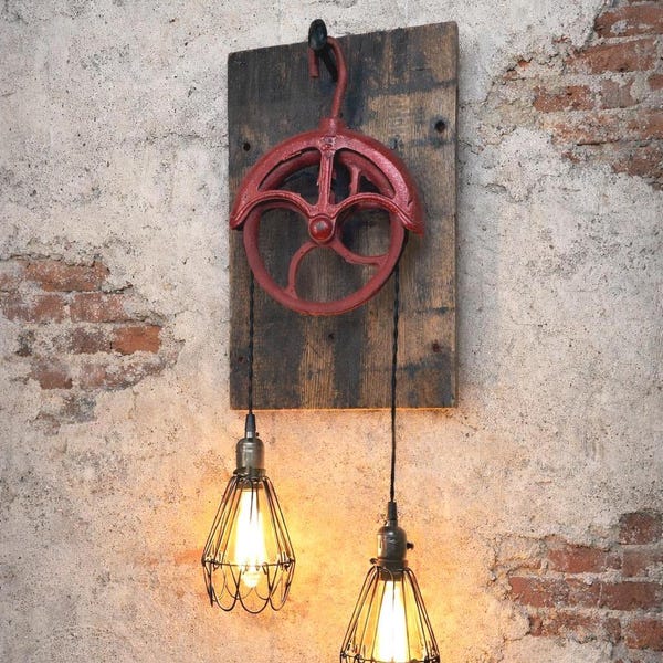 May include: A rustic wall-mounted light fixture featuring a red pulley system attached to a wooden plank. Two pendant lights with wire cage shades hang below, illuminating the space with warm light. The fixture is mounted on a textured, aged wall.