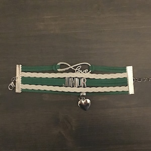 May include: Green and white braided bracelet with a silver infinity charm that says "love" and a silver charm that says "junior" with a silver heart charm hanging from it.