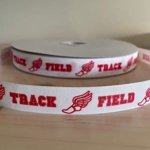 May include: White ribbon with red track and field design. The ribbon has the words "TRACK" and "FIELD" printed on it, along with a red winged foot graphic.