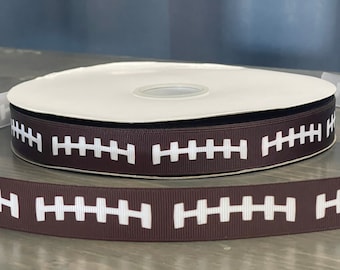 May include: Brown ribbon with white football stitching pattern. The ribbon is wound around a white spool.