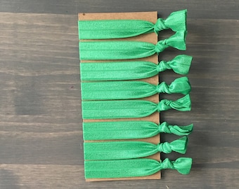 May include: A pack of eight green elastic hair ties. The hair ties are arranged in a row on a brown card.