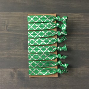 May include: A set of ten green and silver hair ties with a geometric pattern. The hair ties are tied in knots and arranged on a brown card.