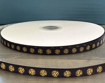 May include: A spool of black ribbon with a gold volleyball pattern. The ribbon is wound around a white cardboard spool.