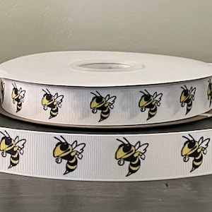 May include: White ribbon with a repeating pattern of yellow and black cartoon bees. The bees are facing left and have a white background.