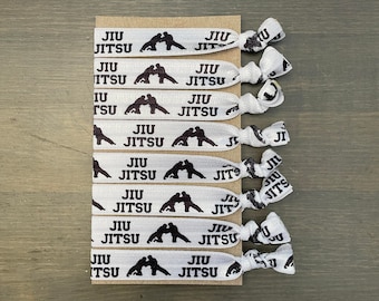 May include: A set of eight white hair ties with the words "JIU JITSU" and a silhouette of two people in a grappling position printed on them.