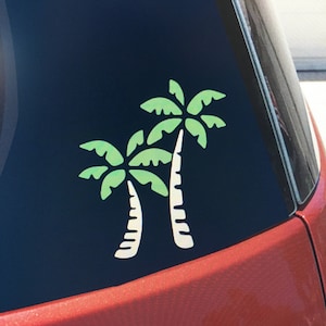 May include: A car window with a green and white palm tree decal. The decal is on the back window of a red car.