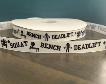 May include: White ribbon with black text and icons that reads "SQUAT BENCH DEADLIFT".