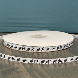 May include: White ribbon with a repeating pattern of black silhouettes of athletes running with wings. The ribbon is rolled up on a white spool.