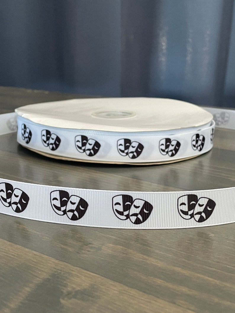 May include: White ribbon with black and white comedy and tragedy masks printed on it. The ribbon is rolled up on a spool.