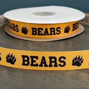 May include: A spool of yellow ribbon with the word "BEARS" printed in black, along with a black bear paw print. The ribbon is on a brown cardboard spool.