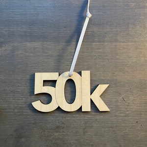 May include: A wooden ornament with the text "50k" on it. The ornament is attached to a white string.