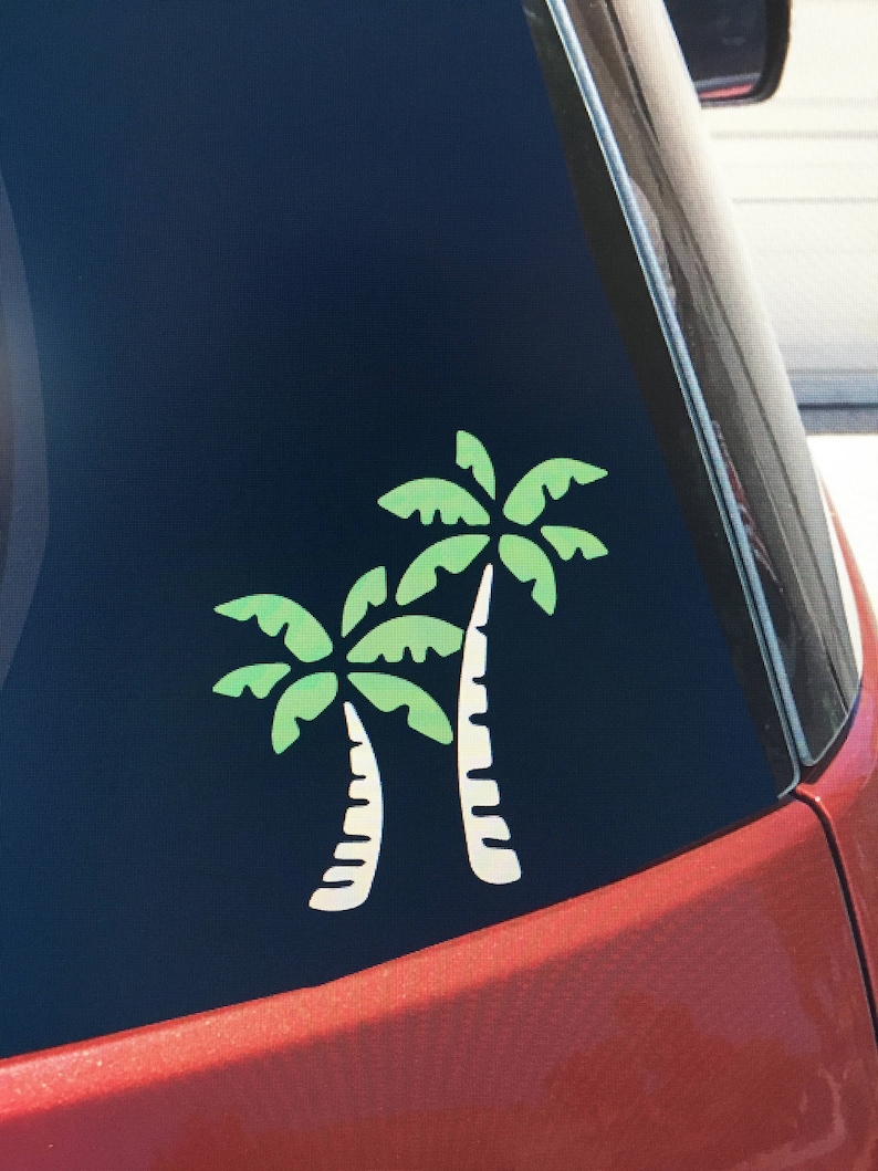 May include: A car window with a green and white palm tree decal. The decal is on the back window of a red car.
