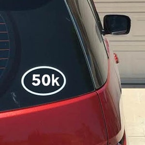 May include: A red car with a white oval sticker that says "50K" on the back window.