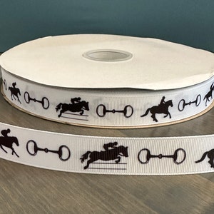 May include: White ribbon with a repeating pattern of black silhouettes of horses jumping over a fence and a horse bit.