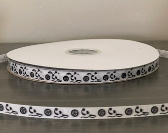 May include: A spool of white ribbon with a black volleyball pattern. The ribbon is wound around a white cardboard spool.