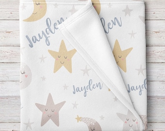 May include: A white baby blanket with a light blue and yellow star pattern. The blanket features a moon and stars with smiling faces. The name "Jayden" is written on the blanket in a light blue cursive font.