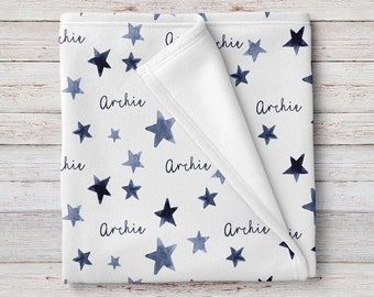 May include: A white baby blanket with a navy blue watercolor star pattern and the name "Archie" repeated throughout.