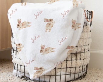 May include: White baby blanket with a repeating pattern of brown bunnies and the name "Julia" in pink script.