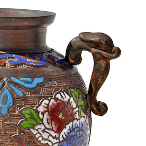 May include: A brown ceramic vase with a dragon-shaped handle. The vase is decorated with blue, green, and red floral patterns.