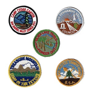 May include: Five embroidered scout patches with different designs. The patches are round and feature various colors, including green, blue, yellow, and red. The patches feature text such as "Camp Cedar Canyon", "San Fernando Valley Council", "Silver Lake Trails", "Treasure Mountain Camp of the Tetons", and "San Mateo County Council".