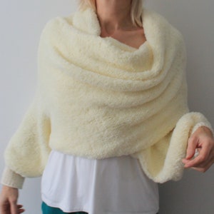 May include: A white fluffy knit shawl with long sleeves. The shawl is draped around the shoulders and the sleeves are gathered at the wrists.