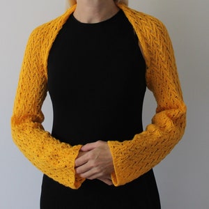 May include: A yellow crocheted shrug with a lacy pattern. The shrug has long sleeves and a wide neckline.