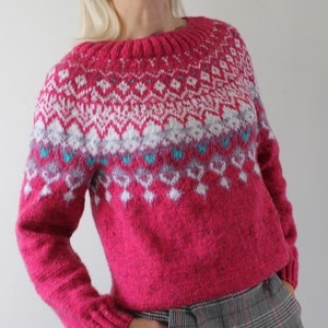 Puede incluir: Un su&eacute;ter rosa con un patr&oacute;n geom&eacute;trico blanco y azul. El su&eacute;ter tiene mangas largas y cuello redondo.