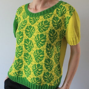 May include: A short-sleeved knitted sweater with a green and yellow monstera leaf pattern. The sweater has a round neckline and a cropped length.