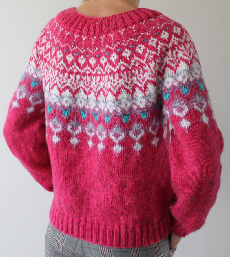 Puede incluir: Un su&eacute;ter de punto rosa con un patr&oacute;n geom&eacute;trico blanco y azul. El su&eacute;ter tiene cuello redondo y mangas largas.