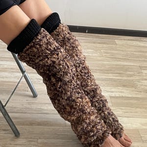 Könnte beinhalten: Ein Paar Beinwärmer mit einem langen, flauschigen, braun und beige gemusterten Kunstfellkörper und einem einfarbigen, schwarzen Rippstrickbündchen am oberen Ende. Die Beinwärmer reichen vom Knie bis zum Knöchel und bedecken die Unterschenkel.