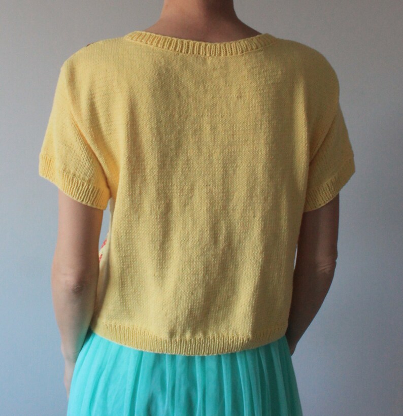 May include: A yellow short-sleeved knitted cardigan with a crew neck. The cardigan is worn over a turquoise tulle skirt.