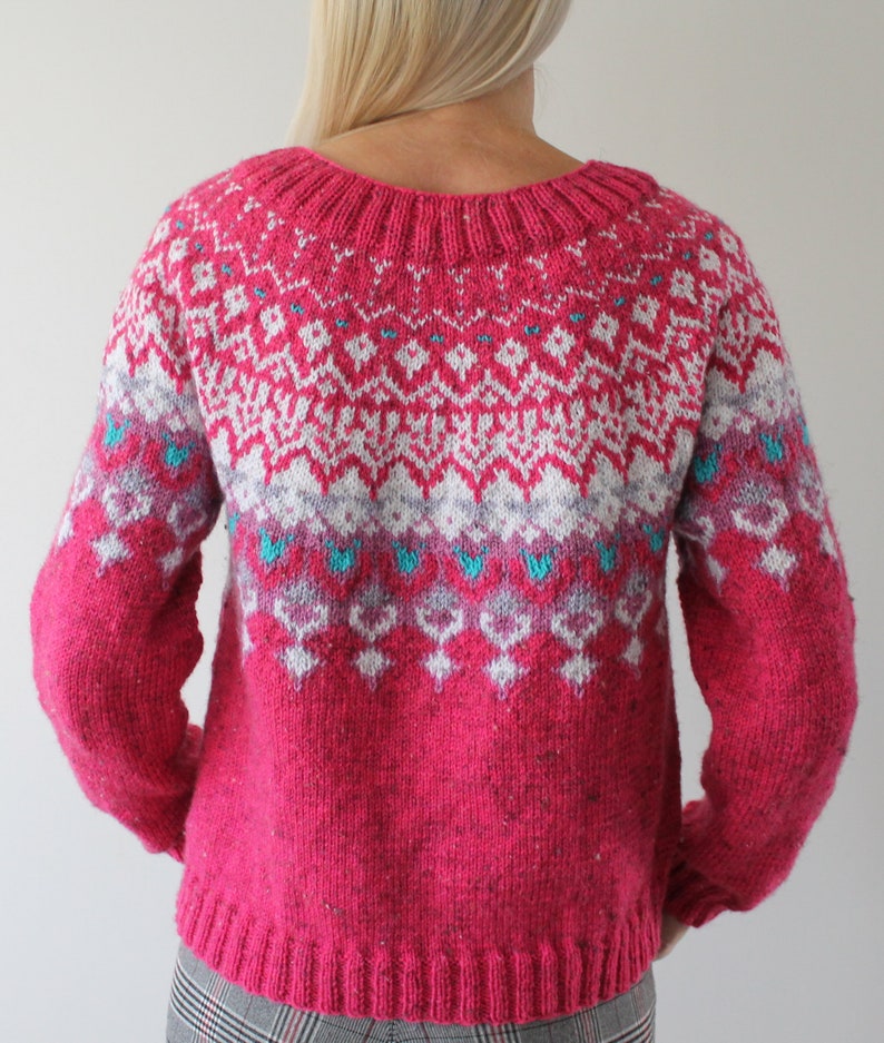 Puede incluir: Un su&eacute;ter de punto rosa con un patr&oacute;n geom&eacute;trico blanco y azul. El su&eacute;ter tiene cuello redondo y mangas largas.